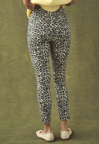 Leopard-print skinny jeans in black and beige, featuring back pockets and a fitted design, paired with light beige flats.