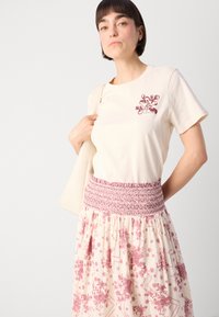 Light beige cotton t-shirt with a burgundy floral design on the chest, paired with a flowy cream skirt featuring a pink floral pattern and smocked waist.