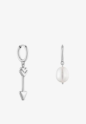 Boucles d’oreilles créoles en argent avec un pendentif flèche suspendu sur l’une et une perle blanche unique sur l’autre, toutes deux sur fond blanc.