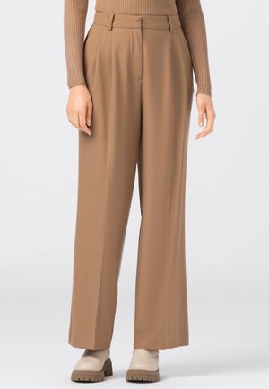 Woman wearing high-waist, wide-leg camel trousers with front pleats, a button and zip closure, paired with beige chunky boots.