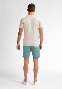 Beige pikétröja med ett texturerat mönster, ihopparad med ljusblå shorts och beiga sneakers. T-shirten har korta ärmar och en krage.