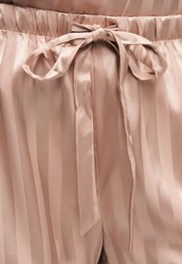 Nærbilde av satengshorts i rosa blush med vertikale striper og knytt sløyfe i elastisk midje.