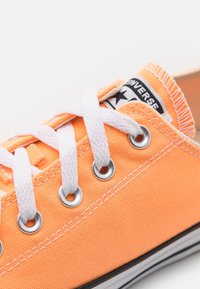 Sneaker in tela arancione con occhielli, lacci e cuciture bianchi. Presenta un'etichetta del marchio in bianco e nero sulla linguetta. Design piatto.