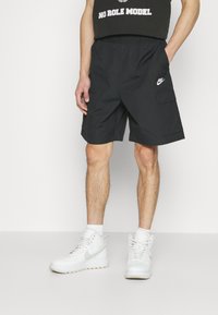 Svarta cargo shorts med elastisk midja, sidfickor och en liten vit Nike-logotyp. Bärs med vita högstövlar.
