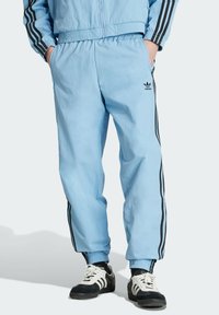 Light blue athletic pants with black side stripes, elastic waistband, and cuffs. Features a small black Adidas logo on the front.