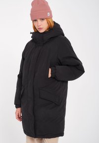 Zwarte geïsoleerde jas met een hoge kraag, rits aan de voorkant en twee grote zakken. Heeft elastische manchetten en een gladde, matte textuur.