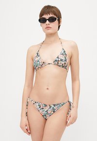 Kwiatowy bikini z trójkątnym stanikiem i wiązanymi bokami. Charakteryzuje się mieszanką pastelowego różu, zieleni i niebieskiego na czarnym tle.