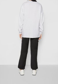 Grå långärmad skjorta och svarta cargobyxor med elastiska mudd och sidofickor, ihopparat med vita sneakers. En enkel, avslappnad outfit.