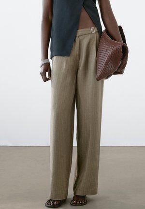 Pantaloni beige chiaro a gamba larga con sottili righe, realizzati in un tessuto strutturato. Abbinati a una maglia scura e a una pochette intrecciata marrone.