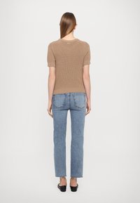 Brun randig stickad t-shirt med kort ärm, kombinerad med ljusblå raka jeans. Enkel, avslappnad design med minimal detaljering och en ren finish.