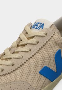 Baskets en toile beige avec un logo V en caoutchouc bleu. Dotées de lacets ronds et d'une languette rembourrée. Surface texturée avec des détails cousus.