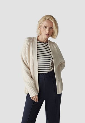 Light beige cardigan with ribbed texture, open front, and long sleeves, paired with a navy high-waisted trouser and striped top.
