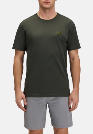 Uomo che indossa una t-shirt verde scuro a maniche corte con logo del sole sul petto e pantaloncini grigio chiaro fino al ginocchio, in piedi con le braccia rilassate.