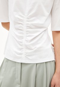 Witte katoenen t-shirt met gathering aan de achterkant, korte mouwen en een ontspannen pasvorm, gecombineerd met een lichtgroene geplooide rok.