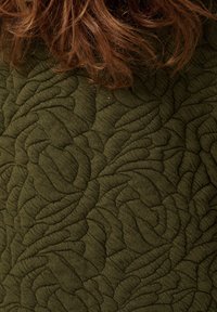 Gestructureerde olijfgroene stof met een verhoogd geblokt patroon dat lijkt op organische vormen. Zacht, rekbaar materiaal met een gedetailleerd ontwerp.