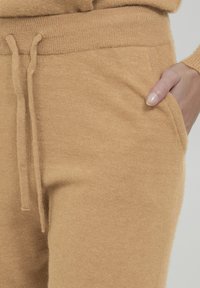 Beige strikjoggere med en blød tekstur, elastisk talje og justerbar snøre. Har sidelommer for bekvemmelighed.
