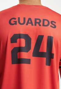 Rød idrettsdrakt med "GUARDS" og nummeret "24" i stor svart skrift på baksiden. Laget av pustende mesh-stoff.