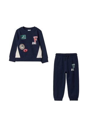 Marineblauw kindervoetbalshirt- en broekset met witte zijpanelen op het shirt en sportthema-patches op beide delen.