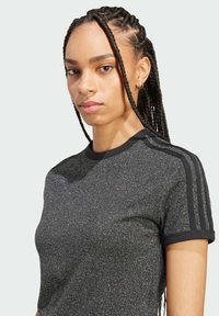 Černé sportovní tričko s třpytivou texturou, krátkým rukávem a černým žebrovaným límečkem. Obsahuje tři černé pruhy na ramenou a logo.