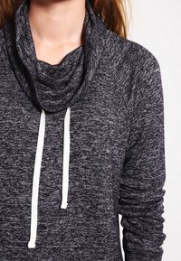 Mörkgrå polotröja med en texturerad tyg. Har vita dragsnören och långa ärmar med ribbade detaljer.