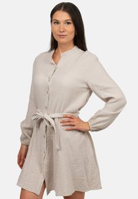 Abito button-up beige chiaro con tessuto testurizzato, maniche lunghe e vita cintata. Presenta un colletto e uno spacco laterale per stile.