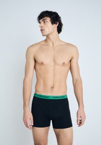Black boxer briefs with a green waistband labeled "BJÖRN BORG." The fabric appears smooth and stretchy, with a close-fitting design.