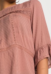 Haut rose avec tissu texturé, doté de manches à volants, d'une bordure en dentelle délicate et d'une coupe ample.