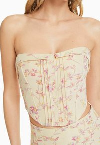 Top bez ramínek z jemně žluté látky, zdobený květinovými potisky v růžové a fialové barvě, s plisovanými detaily a přiléhavým střihem.