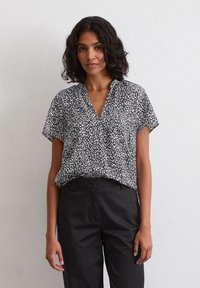 Short-sleeve blouse featuring a black and white speckled pattern, a v-neckline, and a loose fit, paired with black trousers.