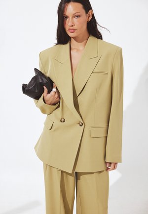 Dvojradový, svetlý khaki blejzer s prehnanými ramienkami, jednou náprsné vrecko a zlatými gombíkmi. Spárované s ladnými nohavicami.
