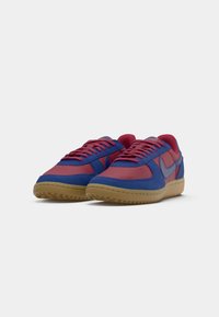 Sko med en blå og rød tekstiloverdel, der har et low-top design, gummisole i naturlig farve samt kontrasterende snørebånd og sømdetaljer.