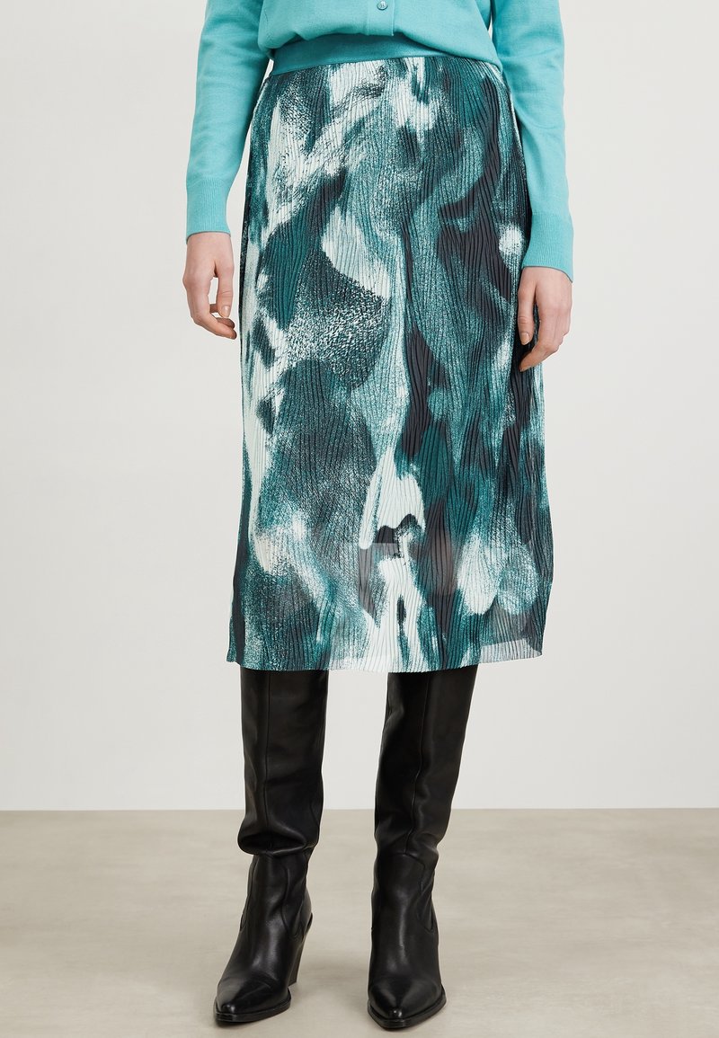 Jupe midi avec un imprimé abstrait multicolore en bleu-vert, noir et blanc, avec une texture plissée. Portez-la avec des bottes noires à hauteur de genou.