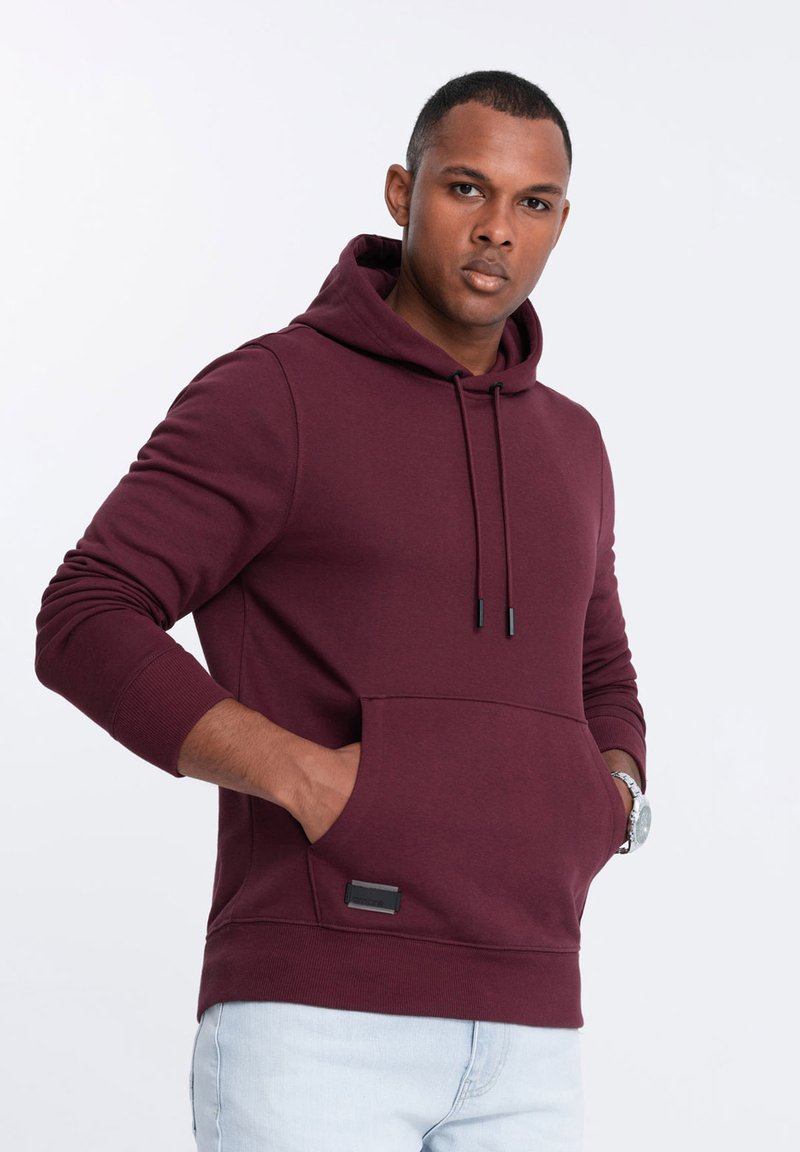 Felpa bordeaux con tasca a canguro, cappuccio con lacci e polsini a coste. Presenta un piccolo logo nero sul davanti. Realizzata in materiale morbido.