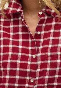 Camicia di flanella a quadri rossi e bianchi con colletto, chiusura con bottoni e taschino sul petto. Tessuto morbido e design a quadri classico.