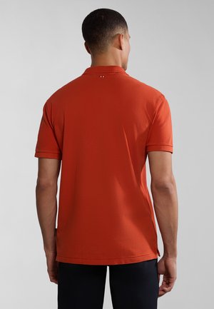 Kortærmet polo i orange stof, med krave, syede detaljer og sideskæringer i sømmen for bedre bevægelsesfrihed.