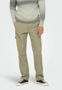 Lysegrøn kordfløjspants med lige ben, parret med en gradient striktrøje. Sorte lavtop sneakers fuldender outfittet.