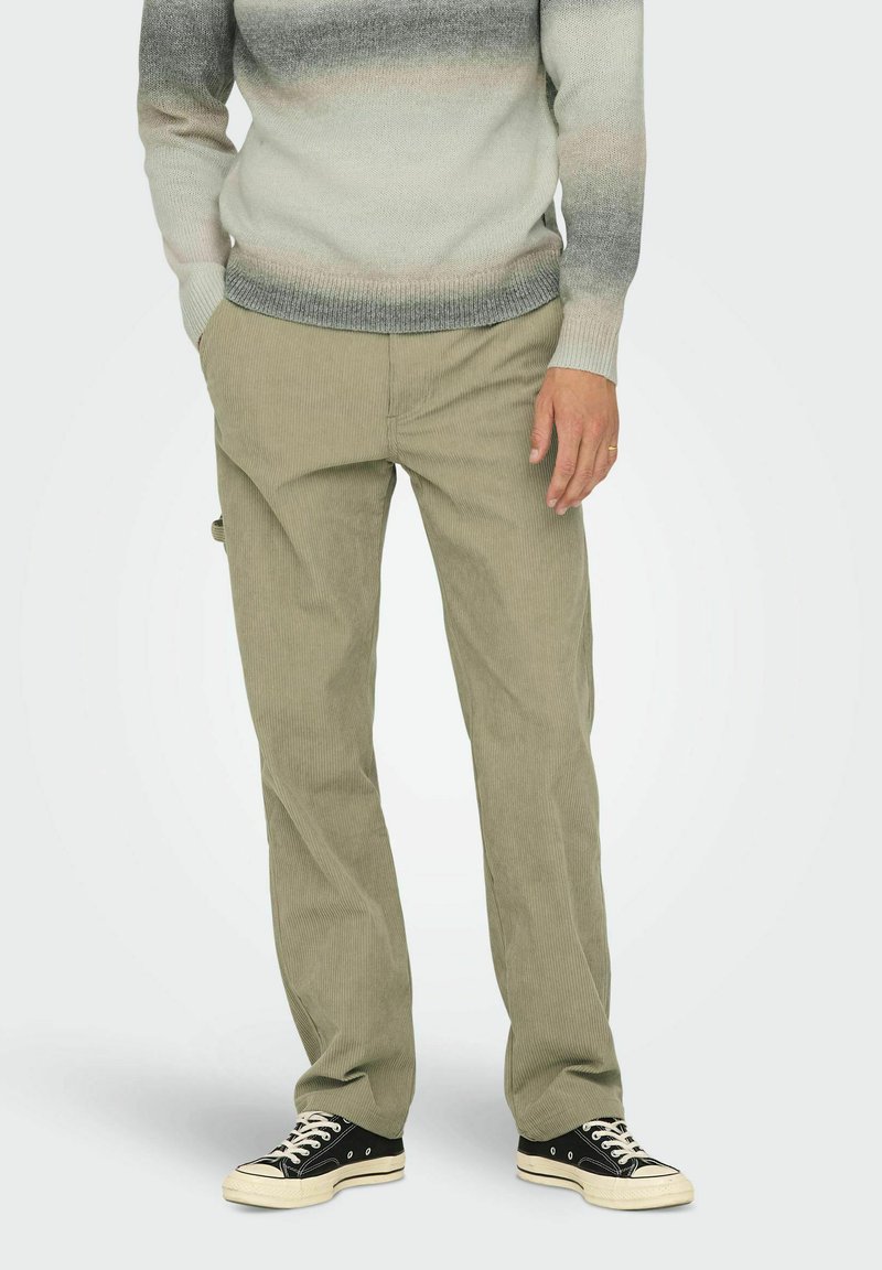 Lysegrøn kordfløjspants med lige ben, parret med en gradient striktrøje. Sorte lavtop sneakers fuldender outfittet.