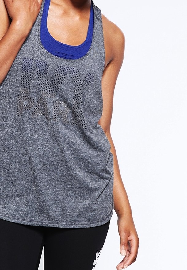 Kvinde iført grå Nike tanktop over blå sports-bh og sorte leggings med hvidt logo, stående mod hvid baggrund.