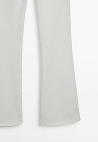 Partie inférieure d’un pantalon évasé gris clair avec couture latérale visible sur fond blanc