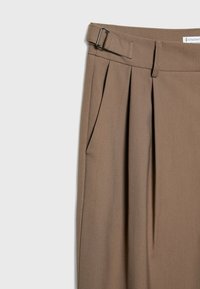 Pantalon marron taille haute avec plis, poche latérale, passants pour ceinture et une boucle réglable en argent sur la ceinture.