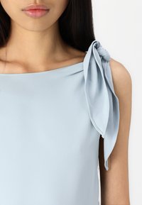 Ανοιχτό μπλε φόρεμα με έναν ώμο και λεπτομέρεια σε κόμπο. Λείο ύφασμα με απαλό άγγιγμα και απλό, κομψό σ�χέδιο.