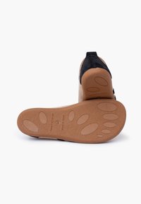 Zapato de ante marrón con tacón negro, mostrando la suela texturizada con patrones ovalados y el texto "Hecho en España". Talla 36.