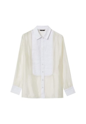 Blusa lunga trasparente a maniche lunghe di colore avorio, con un davanti plissettato bianco, colletto bianco, chiusura con bottoni e polsini bianchi.