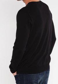 Schwarzer Strickpullover mit rundem Ausschnitt, gerippten Bündchen und Saum. Kombiniert mit blauen Jeans, die eine glatte Textur und eine taillierte Form zeigen.