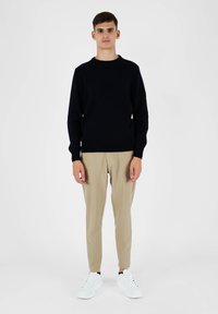 Maglione nero lavorato a maglia con collo rotondo, pantaloni beige su misura e sneakers bianche. L'outfit combina texture e colori solidi.