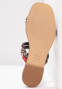 Pärl sandal med ett strukturerat svart rem, dekorativa röda och vita pärlor, och en slät beige gummisula med ett räfflat mönster.