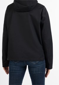 Chaqueta negra con capucha de textura suave, con un diseño corto y costuras laterales, combinada con jeans de denim azul oscuro.