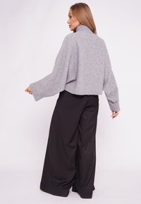 Szary skrócony sweter z wysokim kołnierzem i szerokimi rękawami, zestawiony z czarnymi spodniami w szerokim kroju. Miękka tekstura i luźna sylwetka.