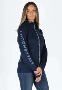 Felpa con zip di colore blu navy, dotata di un cappuccio strutturato, con la scritta "SWEDEMOUNT" in azzurro chiaro sulle maniche, tessuto testurizzato e tasche frontali.