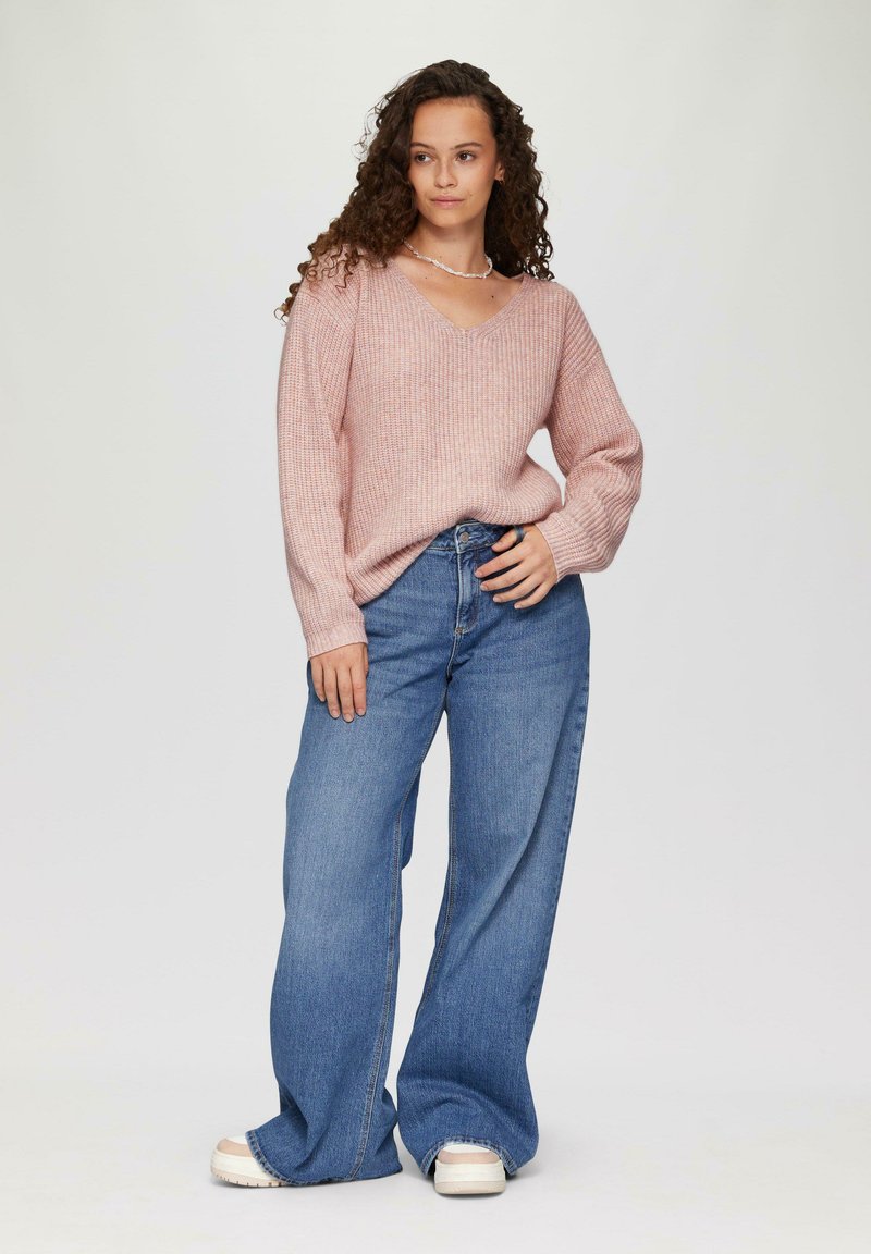 Lichtroze geribbelde trui met V-hals en lange mouwen, gecombineerd met wijde blauwe denim jeans en witte plateau schoenen.